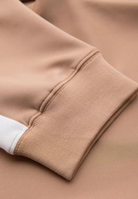 Beige sweatshirt stof met een glad bovenstuk en geribbelde manchetten met een contrasterend witte accent. Gevoel van een gestructureerde weefdetail is evident.
