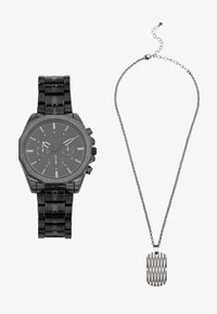 Schwarze Metalluhr mit achteckigem Gehäuse und Chronographenfunktionen, dazu eine silberne Kettenhalskette mit strukturiertem Hundemarke-Anhänger.