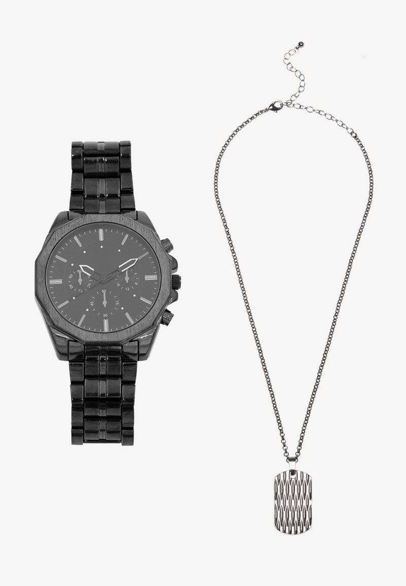 Schwarze Metalluhr mit achteckigem Gehäuse und Chronographenfunktionen, dazu eine silberne Kettenhalskette mit strukturiertem Hundemarke-Anhänger.