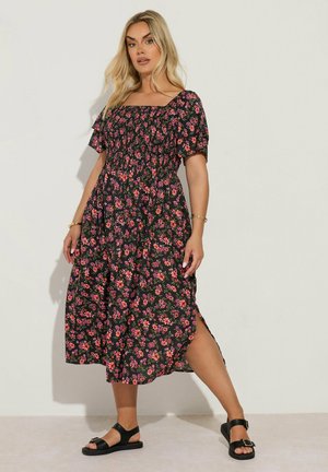 Donna che indossa un abito midi nero con stampa floreale rosa e arancione, scollo quadrato, maniche corte e spacco laterale, abbinato a sandali neri.