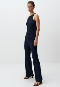 Top in maglina a coste blu navy e pantaloni a palazzo abbinati; design semplice, top senza maniche, texture liscia, con sandali neri con tacco.