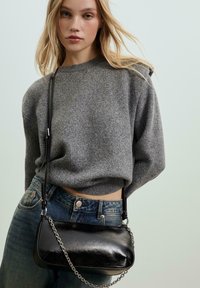 Černá kožená kabelka se stříbrným řetízkem, hladký povrch a kompaktní design. Nosit s šedým svetr a modrými džíny.