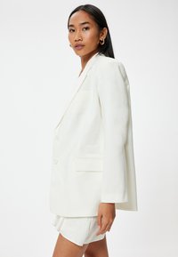 Witte oversized blazer met een gladde structuur, enkelgebreide ontwerp, twee knopen en een borstzak, gecombineerd met bijpassende shorts.
