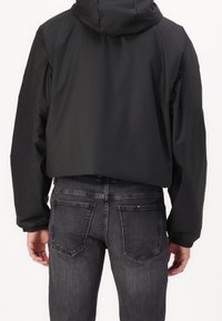 Schwarze, kurze Jacke aus glattem, wasserabweisendem Material mit Kapuze; kombiniert mit dunkelgrauen Denim-Jeans mit Gesäßtaschen.