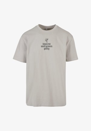 Világosszürke pamut póló kerek nyakkal, fekete felirattal, ami azt írja: "ártatlan, amíg be nem bizonyosodik a bűnössége", és felette egy galamb grafika található.