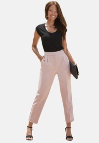 Zwart geribbelde top met korte mouwen, gecombineerd met lichtroze high-waisted broeken. Een zwarte clutch en zwarte hakken met bandjes maken de look compleet.