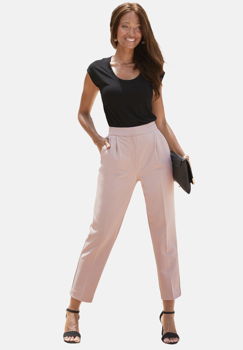 Zwart geribbelde top met korte mouwen, gecombineerd met lichtroze high-waisted broeken. Een zwarte clutch en zwarte hakken met bandjes maken de look compleet.