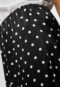 Must tooni pehme kangast seelik, millel on valged laigud. Vöökoht on elastne, mis võimaldab mugavat sobivust ja voolavat siluetti.