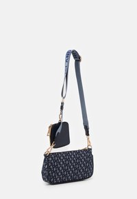 Námořnickomodrá kabelka přes rameno s opakujícím se geometrickým vzorem, zlatými kovovými detaily, odnímatelnou kapsičkou na mince a nastavitelným textilním popruhem.