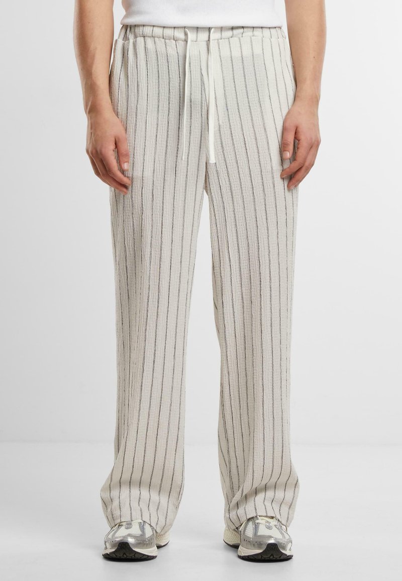 Pantaloni largi de culoare crem cu dungi verticale gri. Realizați dintr-un material texturat, având talie elastică și șnur.