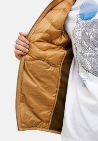 Light brown puffer jacket interior with quilted pattern and a side pocket; soft texture contrasts with white graphic t-shirt underneath.