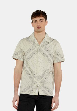Camicia a maniche corte di colore crema con un motivo paisley, caratterizzata da un design diagonale e una chiusura con bottoni. Accento del logo sottile vicino all'orlo.