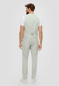 Lichtgroen pak bestaande uit een op maat gemaakte vest met een gespsluiting en bijpassende slim-fit broeken, weergegeven vanuit de achterkant.