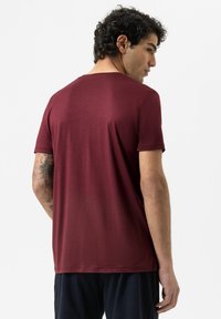 Bordeaux kleurige T-shirt met korte mouwen en een ronde halslijn, zachte textuur en iets getailleerd ontwerp, gezien vanaf de achterkant.