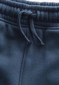 Tumesinised dressipüksid elastse vöökohaga, nöördetailiga ja pehmest, tekstureeritud kangast. Omavad küljetaskuid.