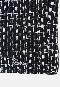 Zwart-wit geweven stof met een getextureerd rasterpatroon en een klein zilver Guess-logo dat nabij de onderhoek is bevestigd.