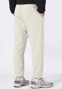Lichtbeige sweatpants met een relaxte pasvorm, elastische tailleband, zijzakken en gestikte details, gecombineerd met grijze sportschoenen.
