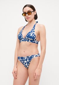 Kék és fehér bikini szett, háromszög alakú melltartóval és alacsony derekú alsó résszel, merész absztrakt mintával; sima anyag és állítható pántok.