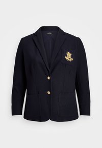 Marineblazer med to frontlommer, gullknapper og et gullbrodert logo på brystlommen. Skreddersydd passform og teksturert stoff.