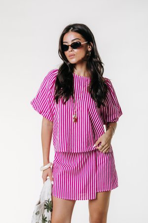 Ružový a biely pruhovaný top s krátkymi rukávmi v kombinácii so zodpovedajúcou mini sukňou. Oblečené s okuliarmi na slnko a držiac vzorovanú tašku na rameno.