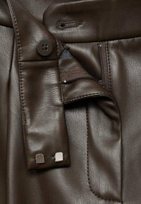 Bruine leren kleding met een knoopsluiting, rits en een gladde textuur met subtiele nerfdetails. Geaccentueerd door metalen hardware.