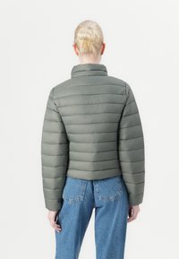 Giacca verde imbottita con motivo a righe orizzontali, colletto alto e design corto, abbinata a jeans in denim blu a vita alta.