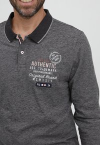 Halli hall sleeves polo särk tumeda kraega ja kontrastse plaketiga. Omab tikitud teksti ja logoga pleki.