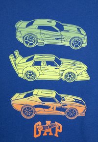 Graphic T-särk, millel on kolm kontuuritud võidusõidumasinat neoonkollases ja oranžis sinisel taustal; sisaldab "Hot Wheels" teksti oranžis.