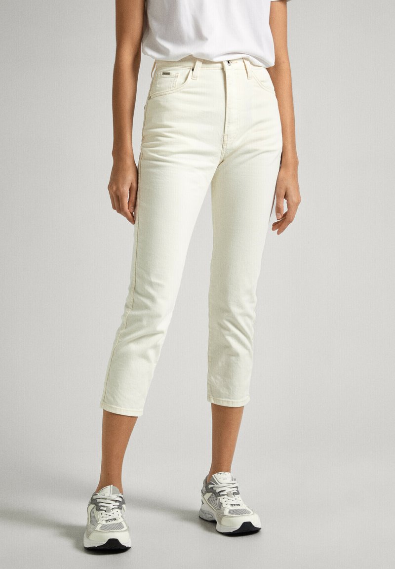 Jeans bianchi a vita alta con un design slim-fit, lunghezza croppata e una texture sottile, abbinati a scarpe da ginnastica bianche e grigie.