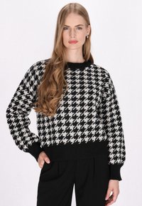 Zwart-wit houndstooth-patroon cropped sweater met lange mouwen en een ribgebreide halslijn en zoom. Gemaakt van een zacht breimateriaal.