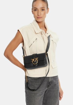 Borsa a tracolla in pelle nera con anello dorato e dettagli a forma di uccello, forma rettangolare, con catena e tracolla regolabile.