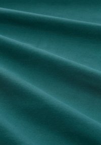 Tessuto di cotone color turchese con una superficie liscia, che presenta pieghe delicate e una sottile lucentezza, creando un motivo a onde.