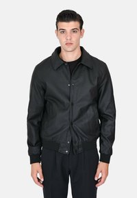 Giubbotto bomber in pelle nera con colletto, bottoni a pressione e tasche laterali. La texture è liscia, con polsini e orlo a coste.