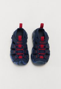 Zapatillas de agua azul marino con acentos rojos, parte superior de malla texturizada, suelas de goma resistentes y cordones y tiradores en rojo contrastante.