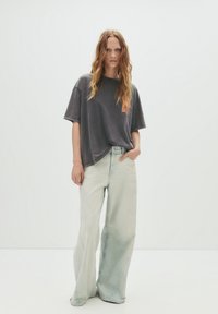 Oversized grå T-shirt med orange grafik og brede letvaskede denimjeans. Outfittet har en afslappet pasform og blødt stof.