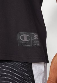 Tricou negru din bumbac, având eticheta cu logo-ul Champion cu detalii gri, poziționată la marginea inferioară. Material texturat cu o finisare netedă.