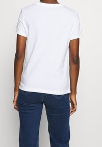 Bílý krátký rukáv tričko s kulatým výstřihem, vyrobené z měkké bavlny, s jednoduchým designem na zadní straně a volným střihem. Nosené s modrými džíny.