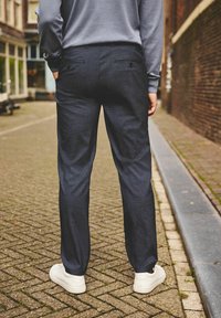 Mariene broek met een getailleerde pasvorm, voorzien van twee achterzakken en een gladde textuur, gecombineerd met witte sneakers.