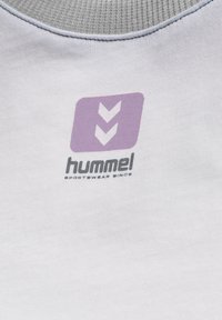 Hvid t-shirt med en grå ribbet krave, med et lilla logo og to nedadgående pile over brandnavnet "hummel" i sort tekst.