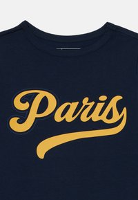 Navyblauwe katoenen t-shirt met een grote gele grafische print die "Parijs" in een gebogen, geschreven lettertype weergeeft, met extra blauwe stikdetails.