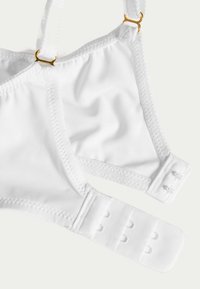 Weißer BH aus elastischem Stoff mit verstellbaren Trägern, goldfarbenen Beschlägen und Haken-Ösen-Verschluss für eine anpassbare Passform.