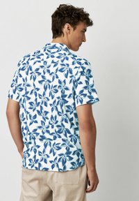 Kurzarmhemd in Weiß mit einem blauen Blumendruck. Verfügt über einen klassischen Kragen und einen lockeren Schnitt, aus leichtem Stoff gefertigt.