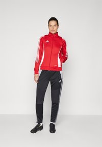 Red zip-up jacket with white accents and three white stripes on sleeves, paired with black sweatpants featuring gray side panels and stripes.