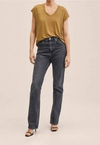 Haut olive à manches courtes associé à un jean taille haute gris foncé et des sandales à talons noires. Texture lisse, coupe décontractée, design simple.