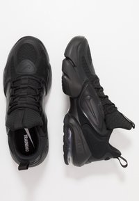 Zapatillas deportivas negras con una parte superior texturizada y acentos lisos, que cuentan con una unidad de amortiguación de aire visible y un tirador en el talón.