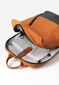 Oranje en grijze rugzak met een ritssluiting, voorzien van een getextureerde binnenkant en een leren band. Inclusief organiser vakken en een ruitpatroon.