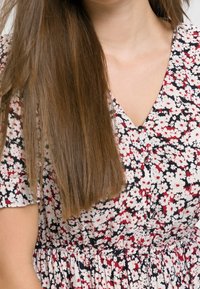 Robe à imprimé floral avec un fond noir orné de fleurs blanches et rouges, col en V, manches courtes et taille élastiquée.