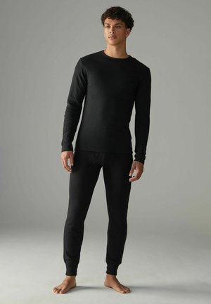 Svart termisk topp och byxor i mjukt, ribbat material. Långa ärmar, åtsittande design och elastiska muddar; sömlös konstruktion, minimal varumärkning.
