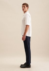 Wit polo shirt met korte mouwen, gecombineerd met donkerblauwe broek en zwarte schoenen. Het shirt heeft een klassieke kraag en zijsplitten voor extra comfort.