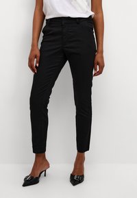 Pantalons noirs ajustés en tissu lisse, dotés de poches latérales et d'une coupe slim, associés à des escarpins noirs à bout pointu.